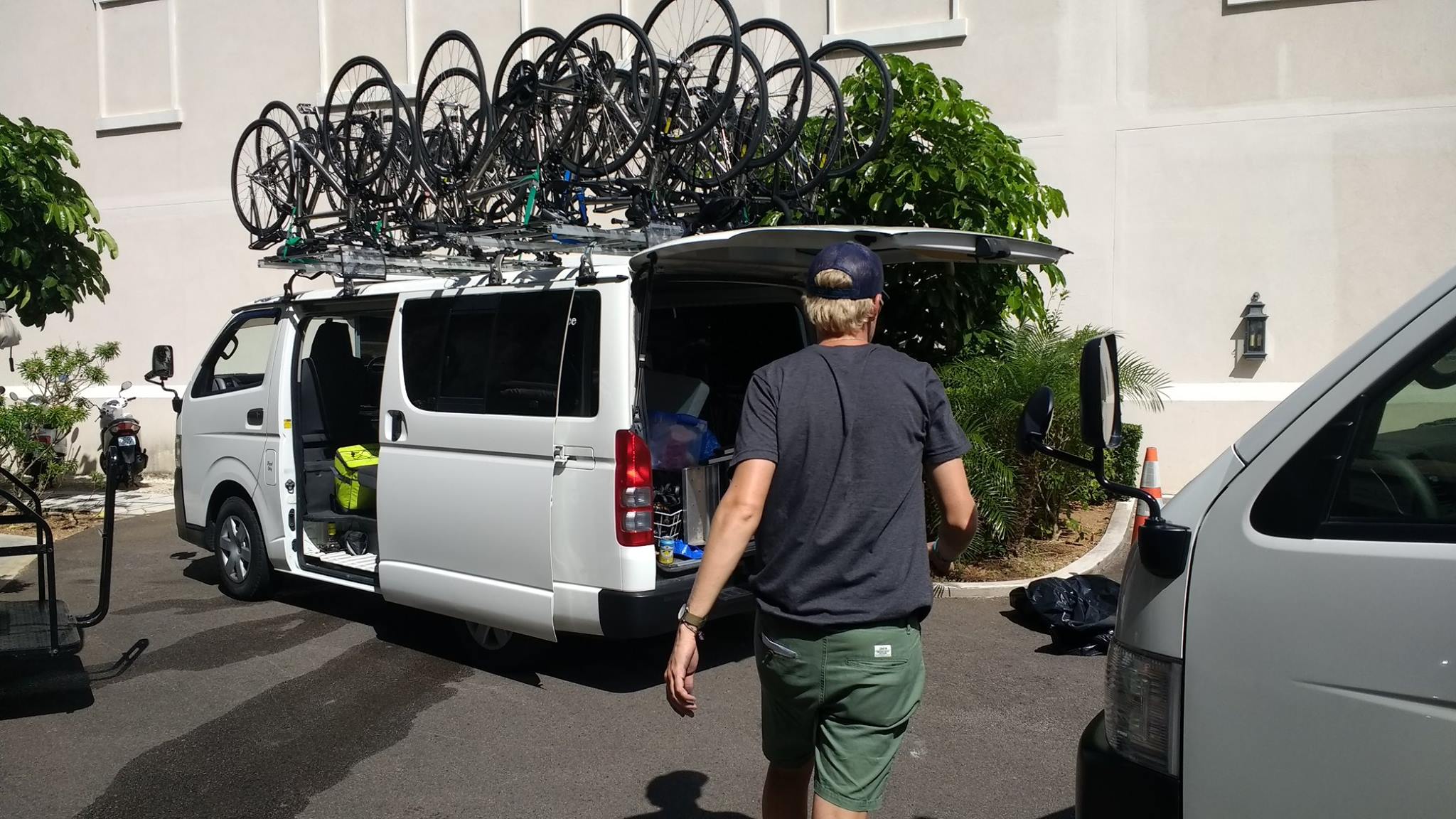 White van with bike racks loaded on top, open trunk, and a person walking nearby.