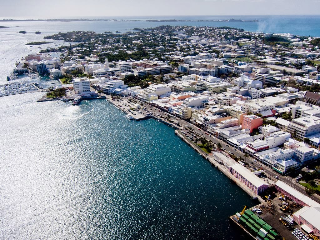 Aerial view of a Bermuda coastal town with white buildings, a vibrant harbor, and sparkling blue waters.