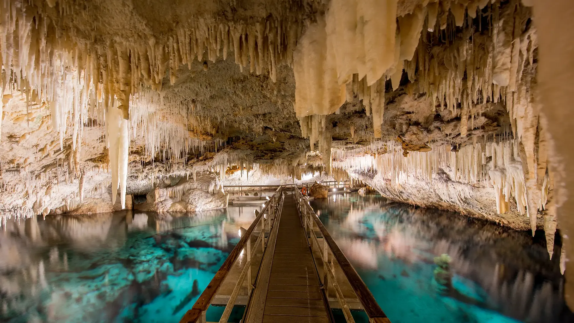 Stunning view of a crystal cave with hanging stalactites and turquoise water.